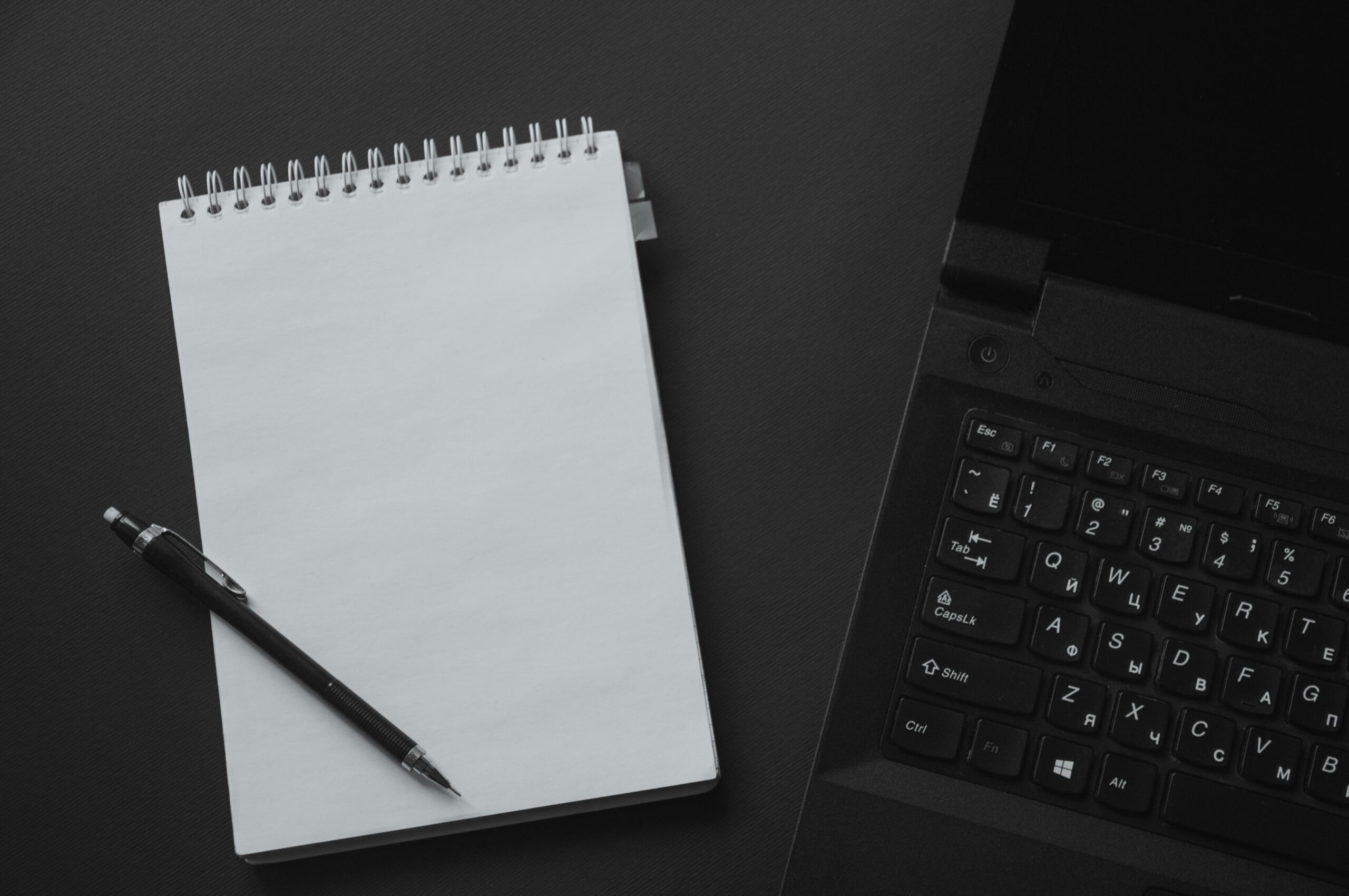 Home Flat lay of an office workspace with a laptop, notepad, and mechanical pencil on a black background.